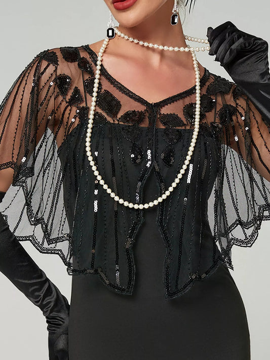 Model wearing a black sheer sequin capelet with a shallow V-neck, floral embellishments and scalloped edges over a black dress