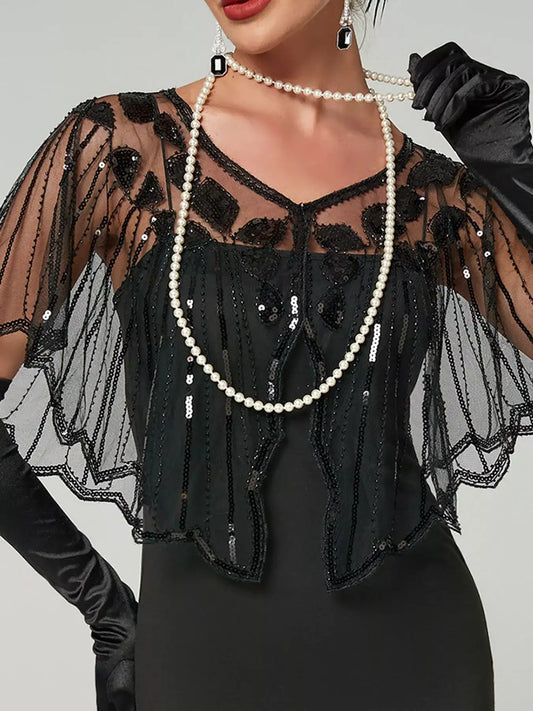 Model wearing a black sheer sequin capelet with a shallow V-neck, floral embellishments and scalloped edges over a black dress