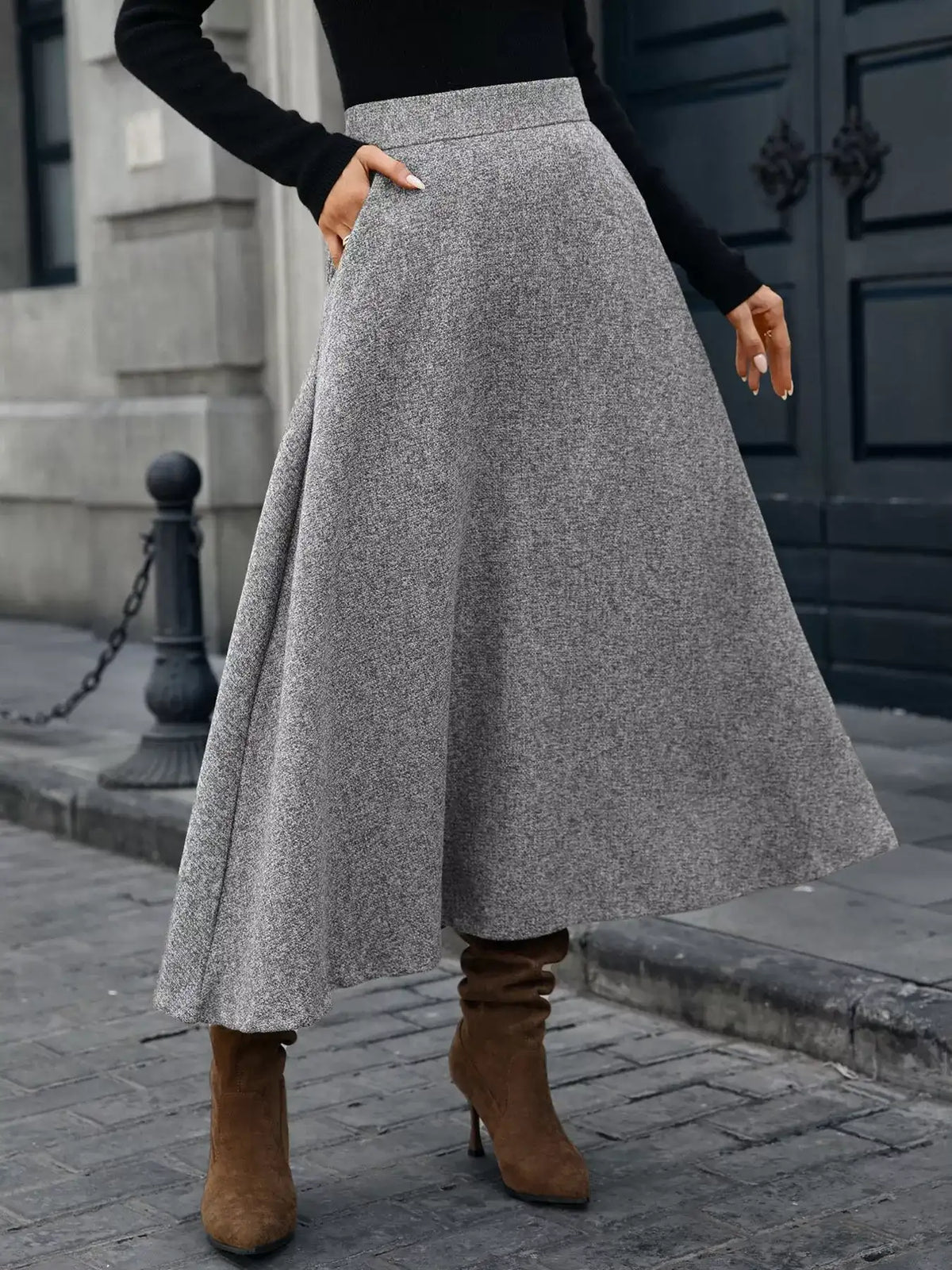 Person wearing a gray skirt and brown boots on a city street.