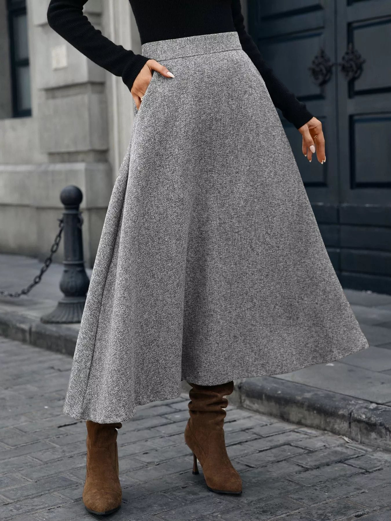 Person wearing a gray skirt and brown boots on a city street.