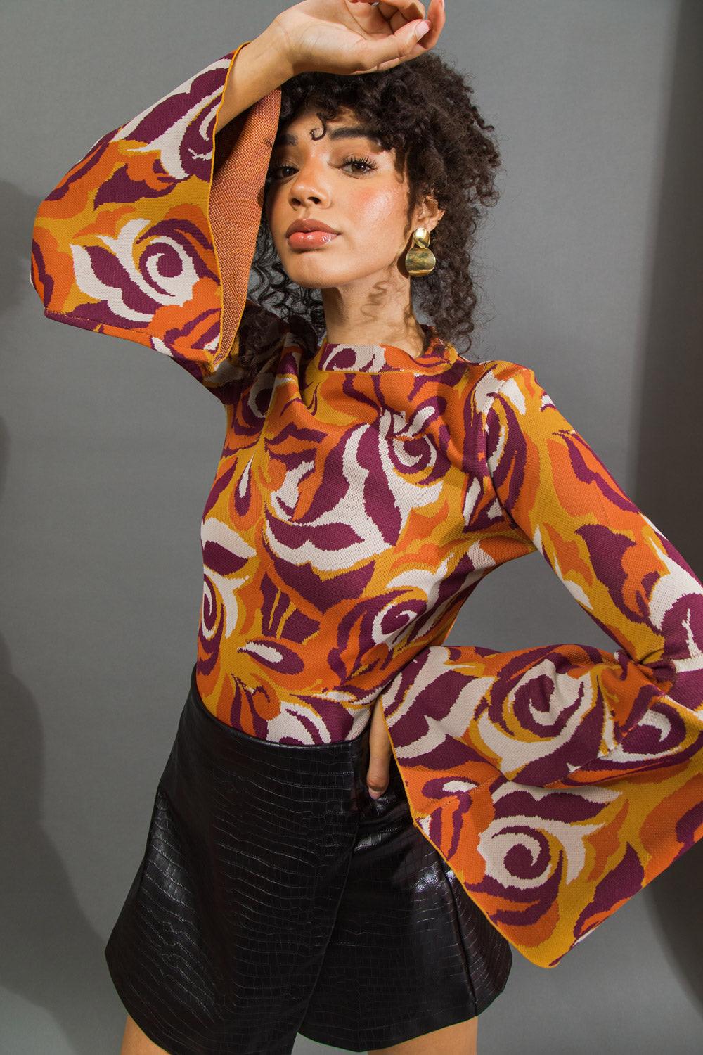 Woman wearing a colorful patterned top with long sleeves against a gray background