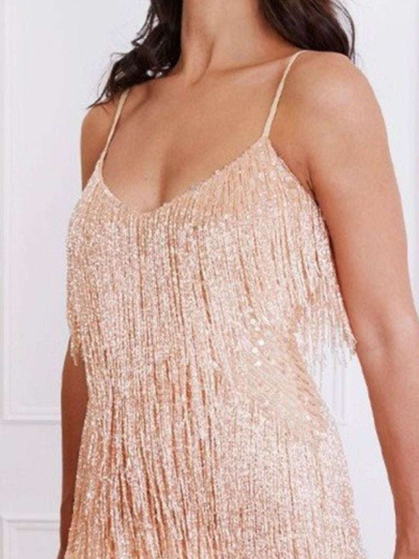 Close-up of a person wearing a sparkly, light-colored dress with thin straps against a white background.
