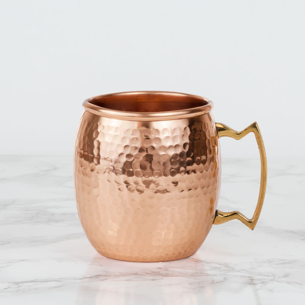 Hammered copper Moscow mule mug with a gold-tone handle on a white marble surface.