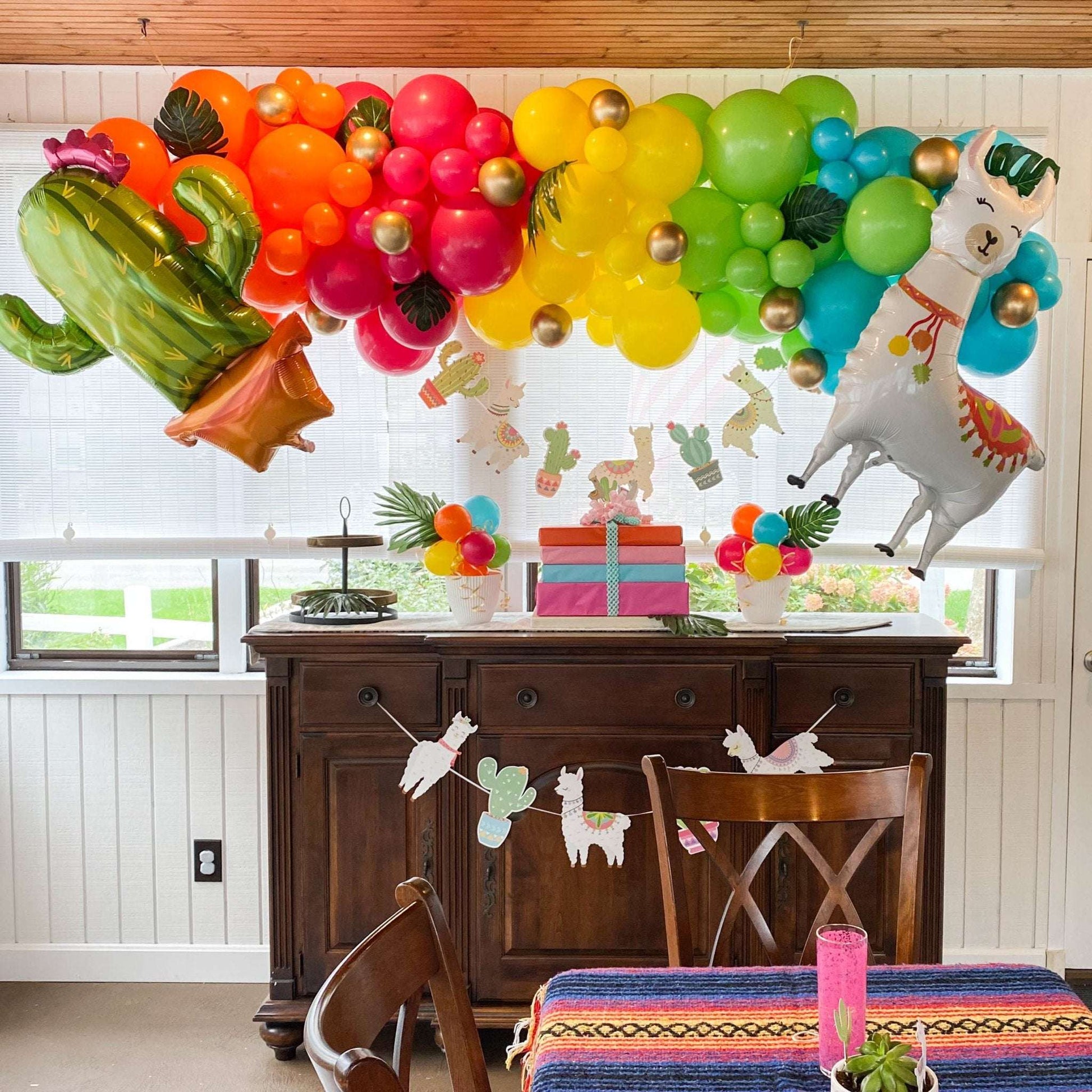 Rainbow balloon garland with cactus and llama foil balloons hanging above a wooden sideboard with llama banners.