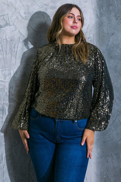 Woman wearing a black sequin top and blue jeans against a textured gray wall.