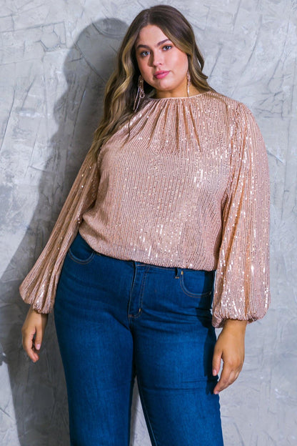 Woman wearing a sparkly beige top and blue jeans against a textured gray wall.