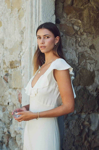 Woman in a white dress holding a glass against a stone wall