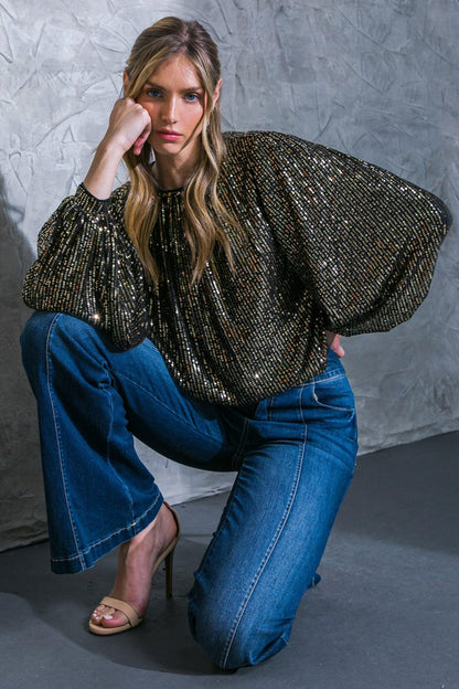 Woman wearing a sparkly top and blue jeans against a gray textured wall.