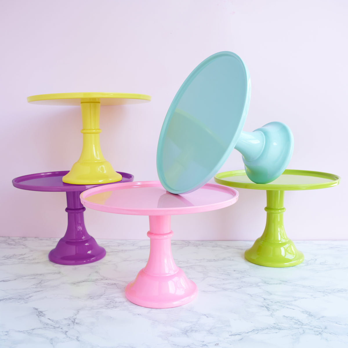 Set of colorful cake stands on a marble surface with a light pink background