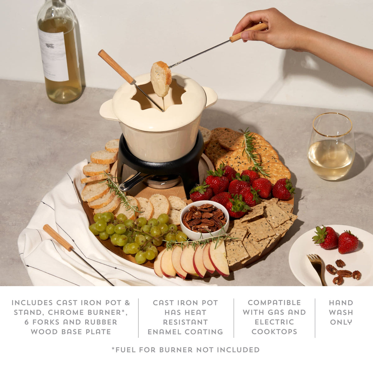 Fondue setup with cheese fondue pot, bread, fruits, and wine on a table.