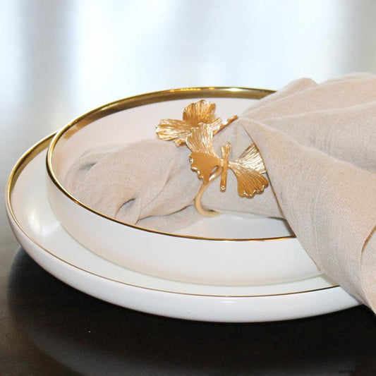 Decorative white dish with gold rim and napkin holder featuring a gold leaf design on a neutral background.