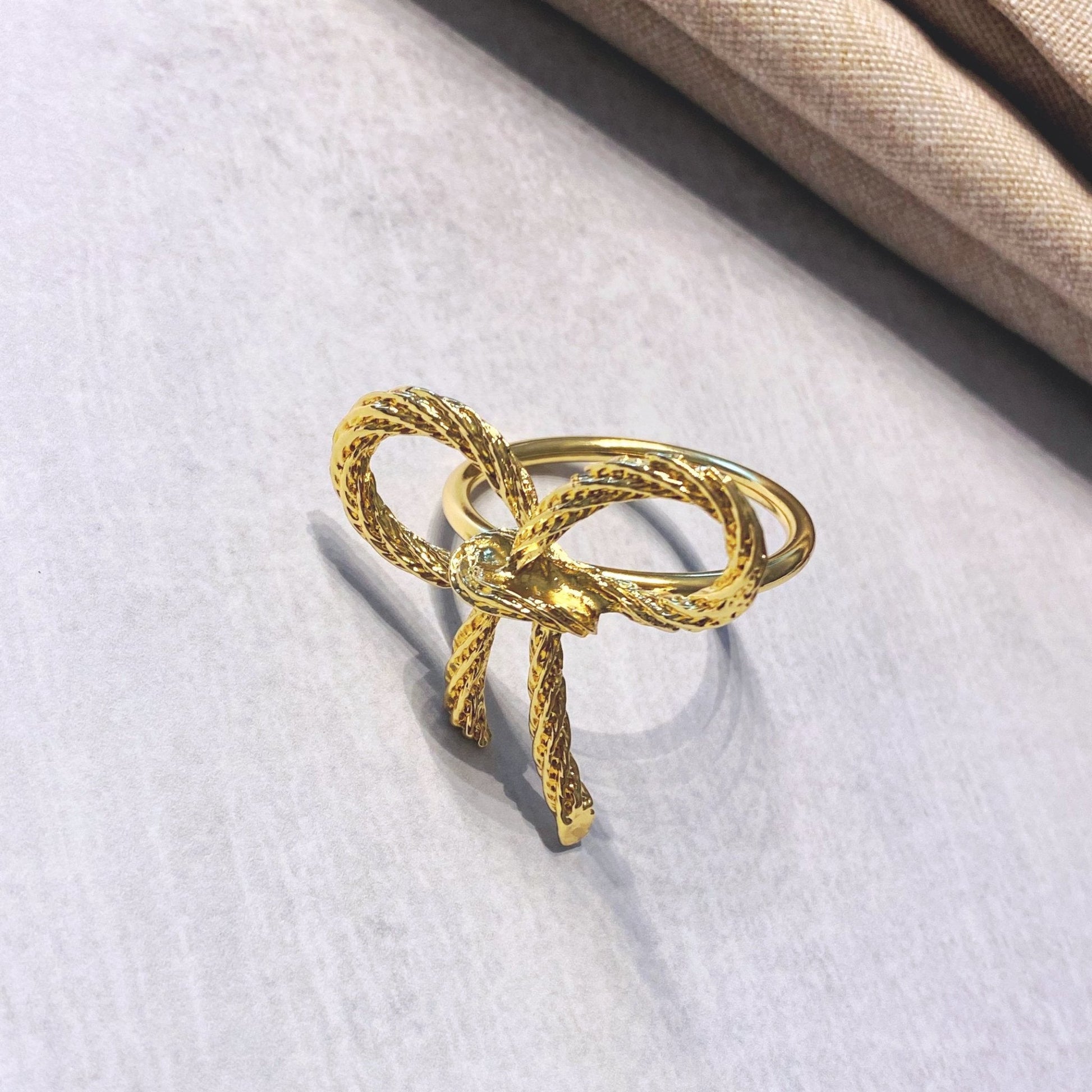 Gold bow-shaped ring on a white fabric background