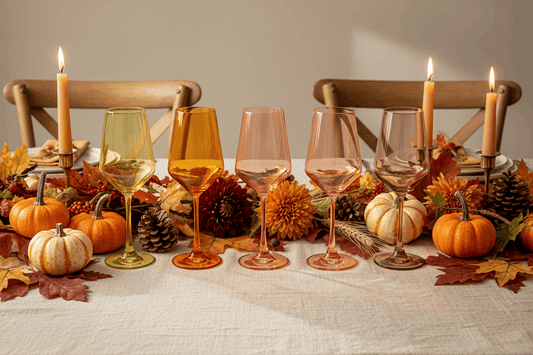 Six colored wine glasses in yellow, orange, peach, and pink shades, arranged in a row against a solid white background.