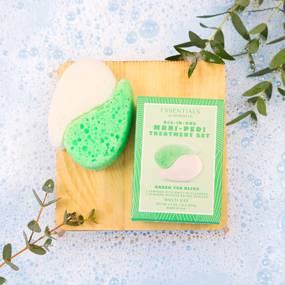 Mani-pedi treatment set with green tea bliss scrub and packaging on a wooden board with eucalyptus leaves.