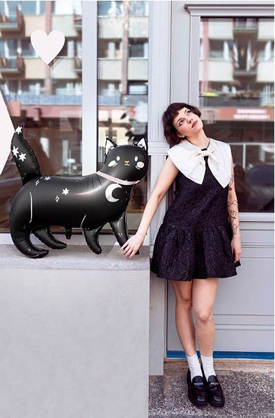 Woman in a black dress with white collar standing next to an inflatable black cat with white stars.