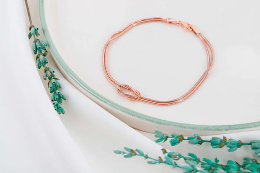 Rose gold bracelet on a white surface with green floral design