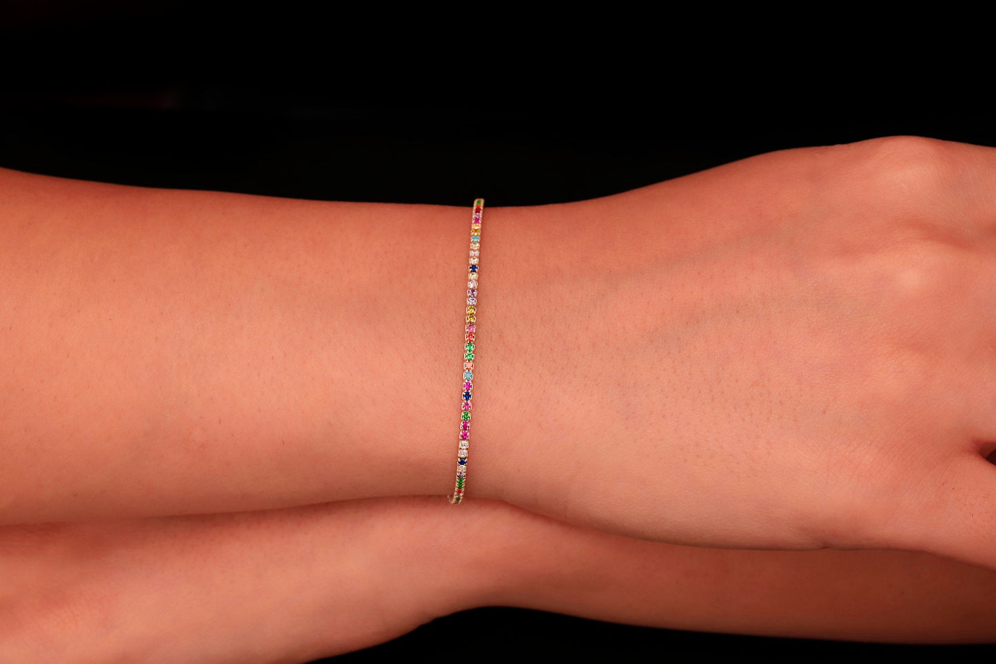Colorful Dreams rainbow bracelet displayed on a wrist, featuring multicolored stones set in a thin gold band.