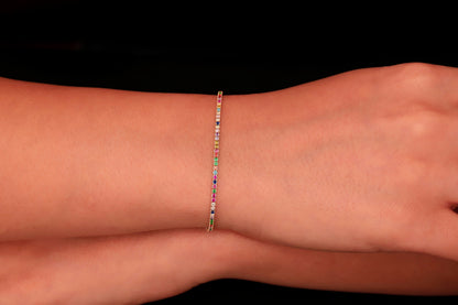 Colorful Dreams rainbow bracelet displayed on a wrist, featuring multicolored stones set in a thin gold band.
