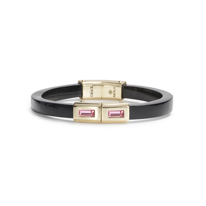 A black enamel bangle bracelet with gold-tone metal accents and rectangular pink baguette-cut crystals, shown on a plain white background.