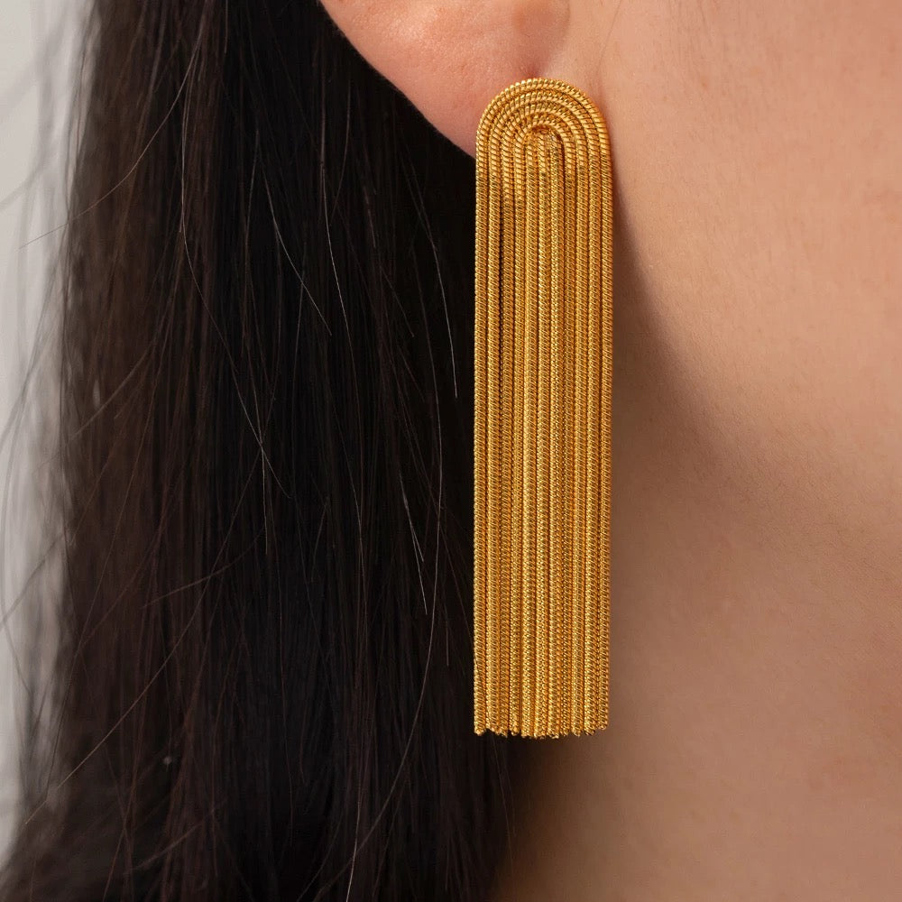 Close-up of an Addison gold fringe earring worn on the ear, showing its rounded top and textured dangling chains.