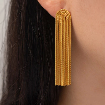 Close-up of an Addison gold fringe earring worn on the ear, showing its rounded top and textured dangling chains.