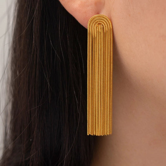 Close-up of an Addison gold fringe earring worn on the ear, showing its rounded top and textured dangling chains.