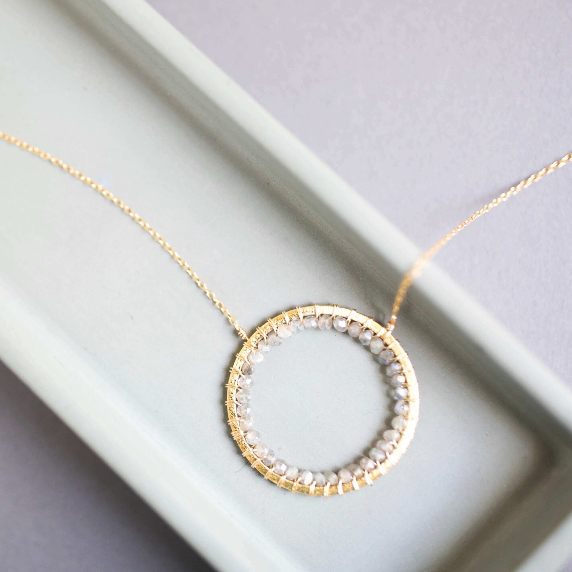 Gold necklace with a circular pendant on a light gray background