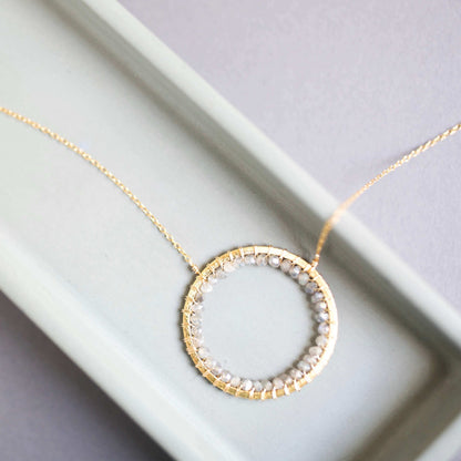 Gold necklace with a circular pendant on a light gray background