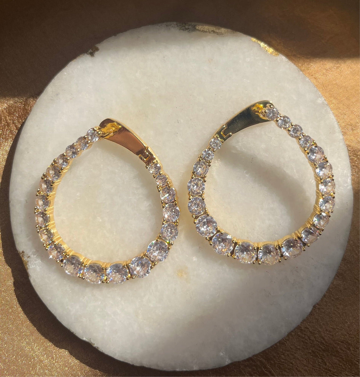 Gold hoop earrings with clear stones on a white stone surface