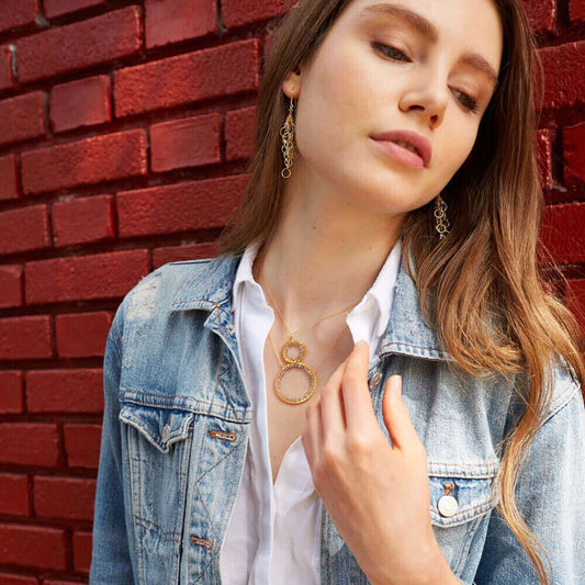 Woman wearing a gold necklace and earrings against a red brick wall
