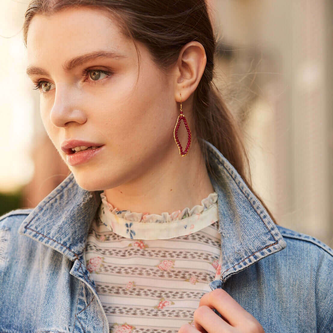 Woman wearing a denim jacket and floral top with a close-up of her earrings.