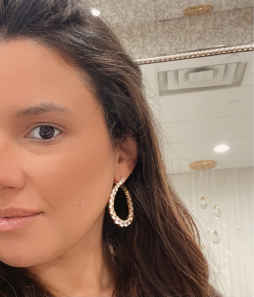 Close-up of a person wearing gold hoop earrings with a blurred background