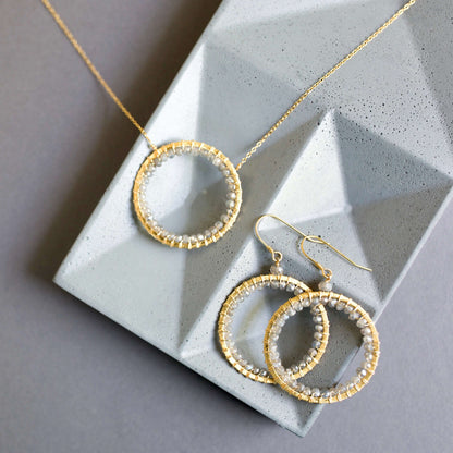 Gold wire-wrapped circular necklace and matching earrings with grey beads on a geometric stone tray.