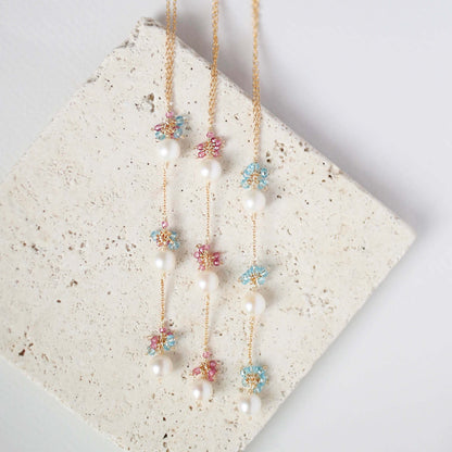 Two floral necklaces with pearls on a textured stone surface