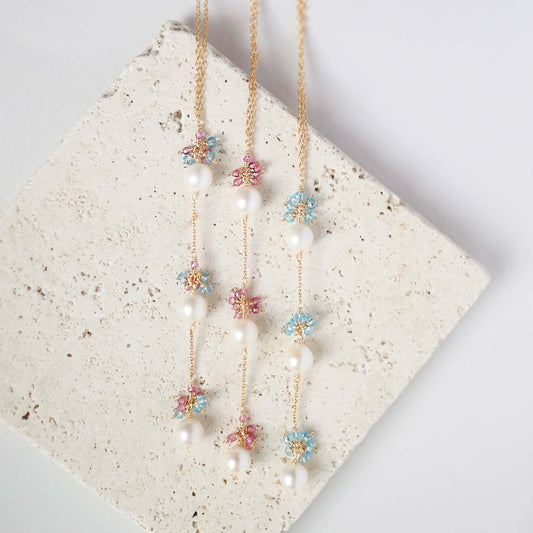 Two floral necklaces with pearls on a textured stone surface