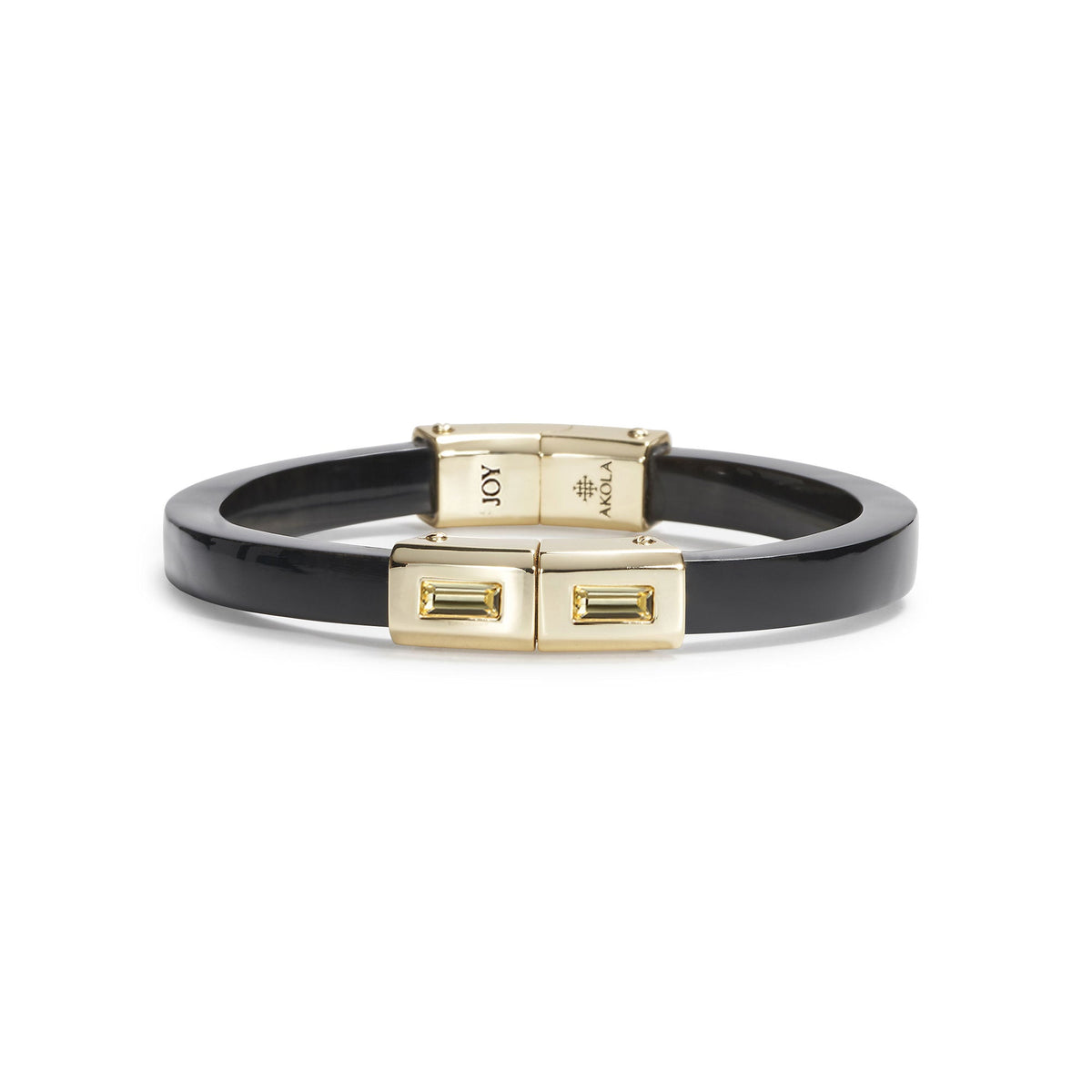 A black enamel bangle bracelet with gold-toned metal hardware, featuring a clasp engraved with 'JOY' and the 'ANNA S. LUX' brand logo, shown on a plain white background.