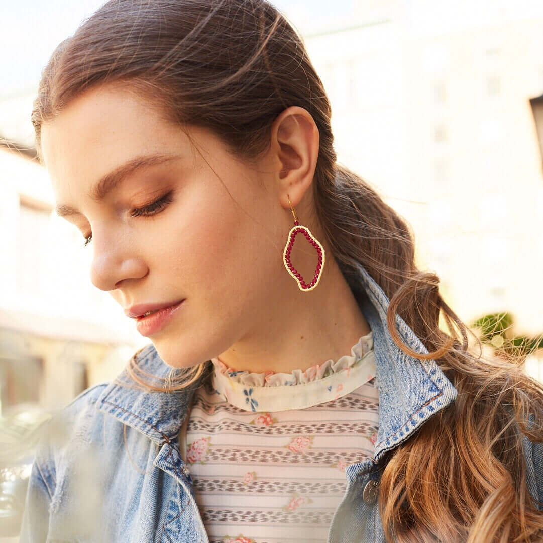 Woman wearing a denim jacket and patterned top with a close-up of her earrings.