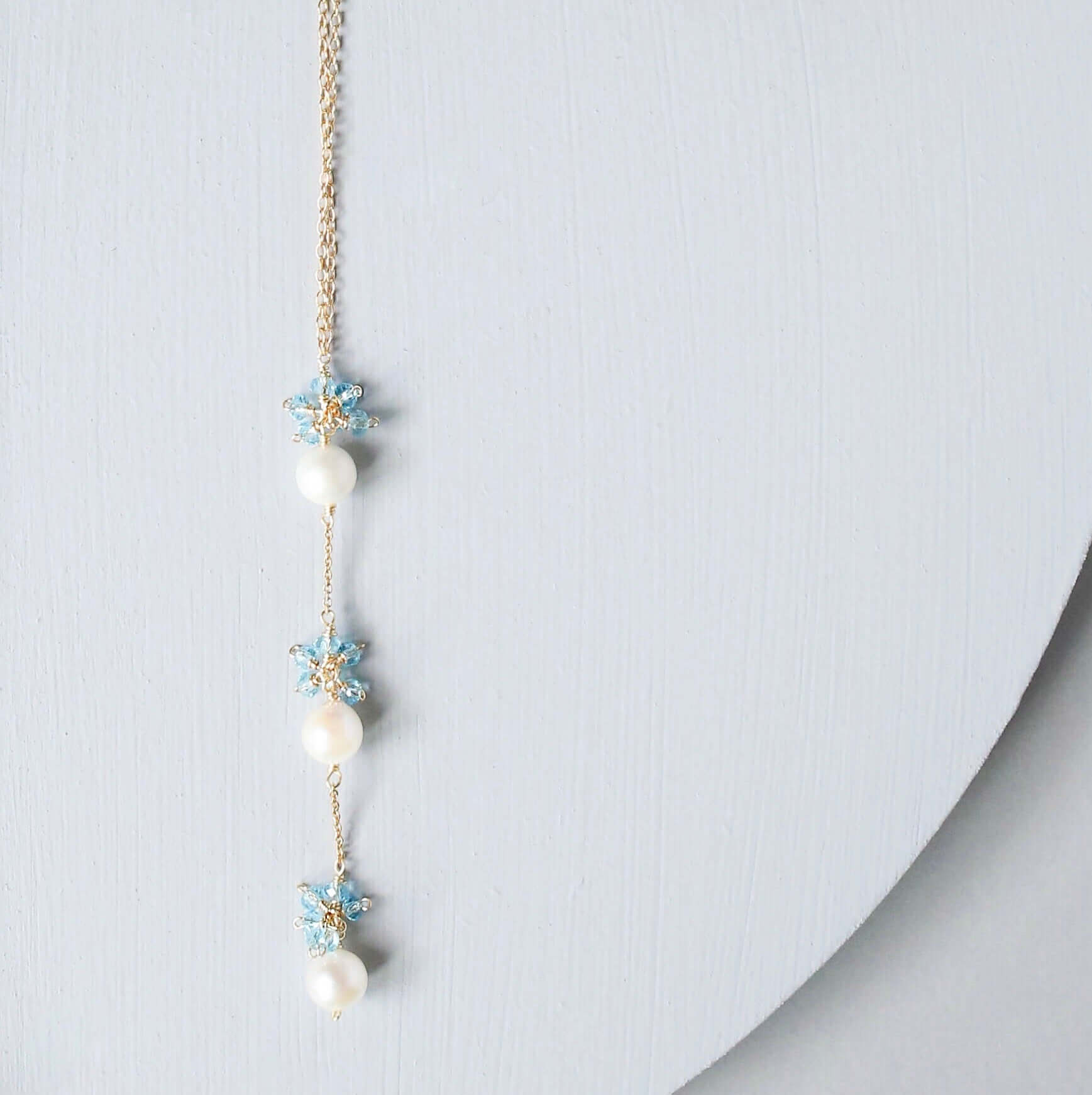 Delicate necklace with pearls and floral elements on a light gray background