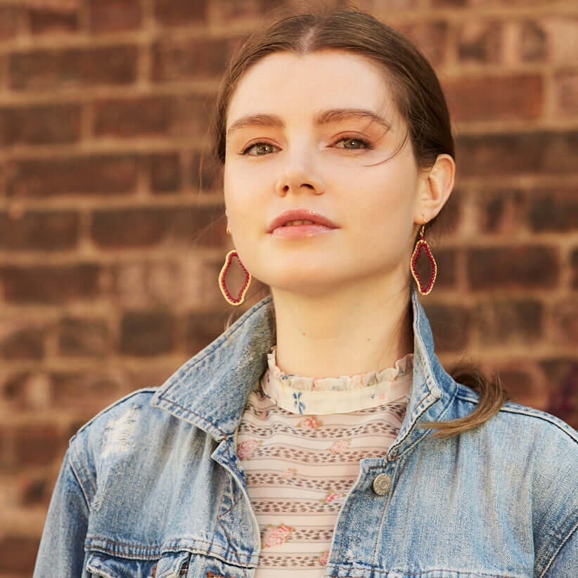 Woman wearing a denim jacket and hoop earrings against a brick wall.