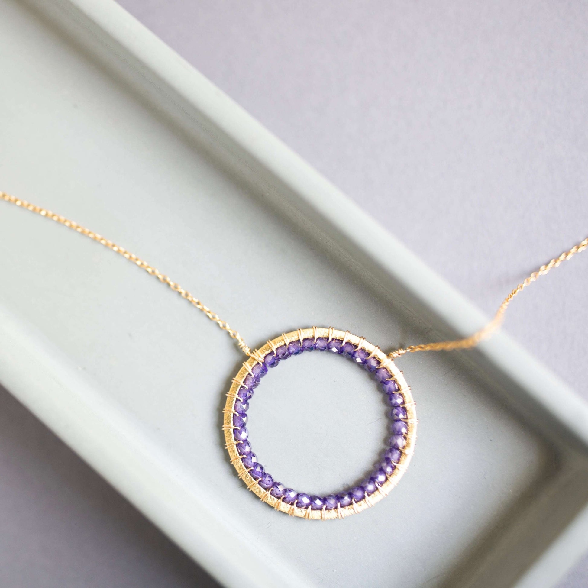 Necklace with a circular pendant featuring purple stones on a light gray background