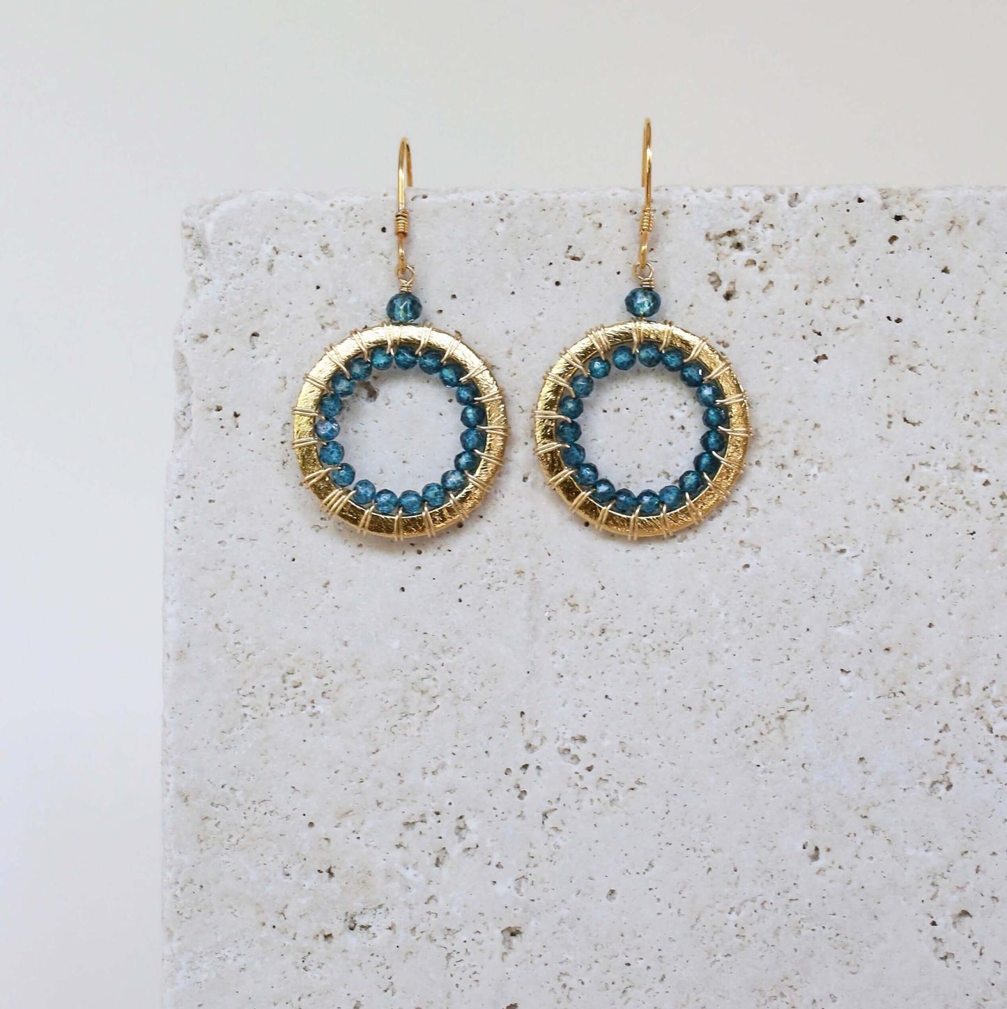 Gold hoop earrings with blue beads on a textured surface