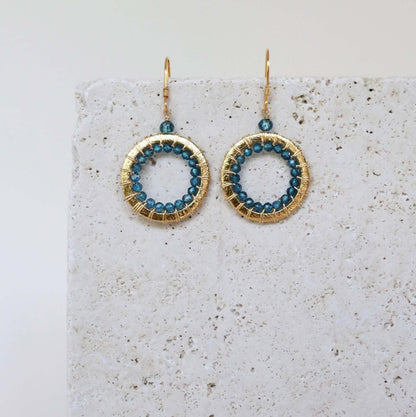 Gold hoop earrings with blue beads on a textured surface