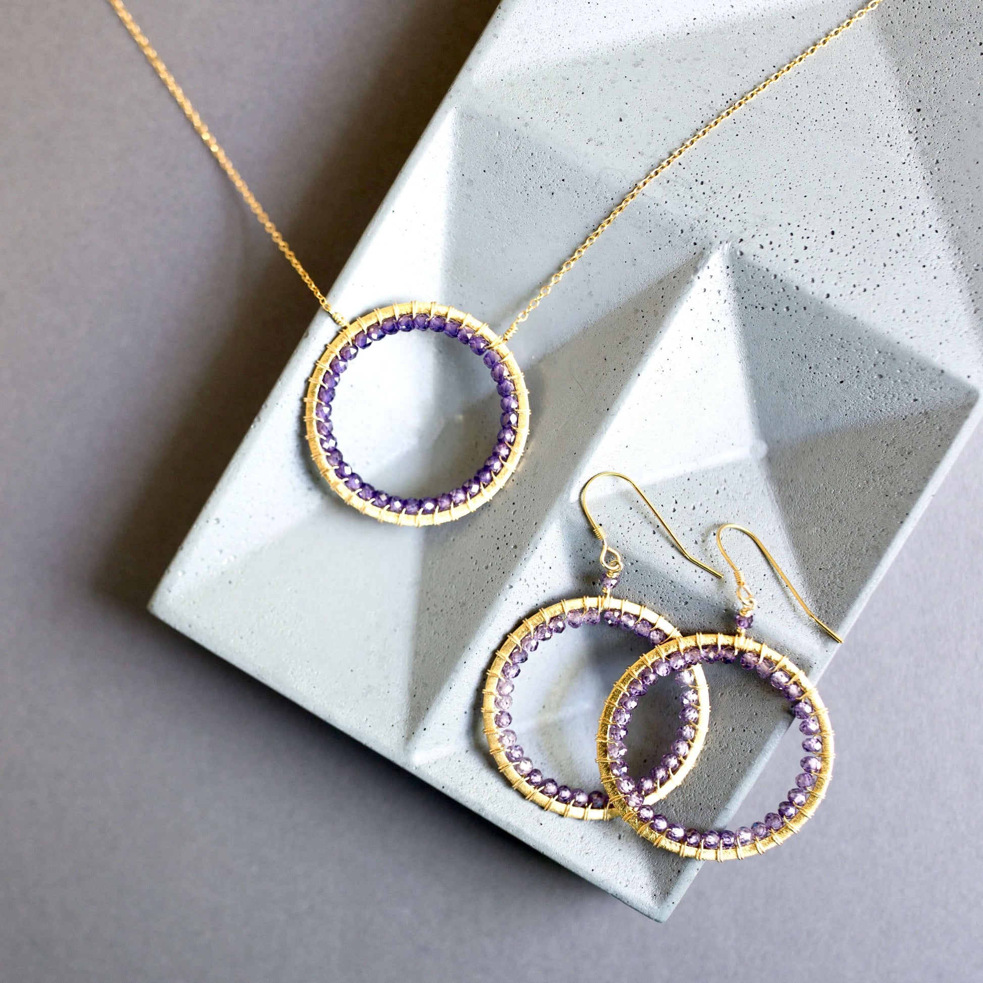 Gold and purple hoop earrings on a textured stone surface