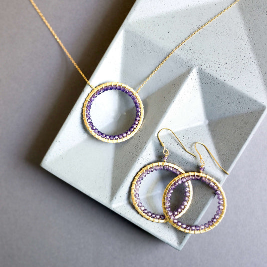 Gold and purple hoop earrings on a textured stone surface