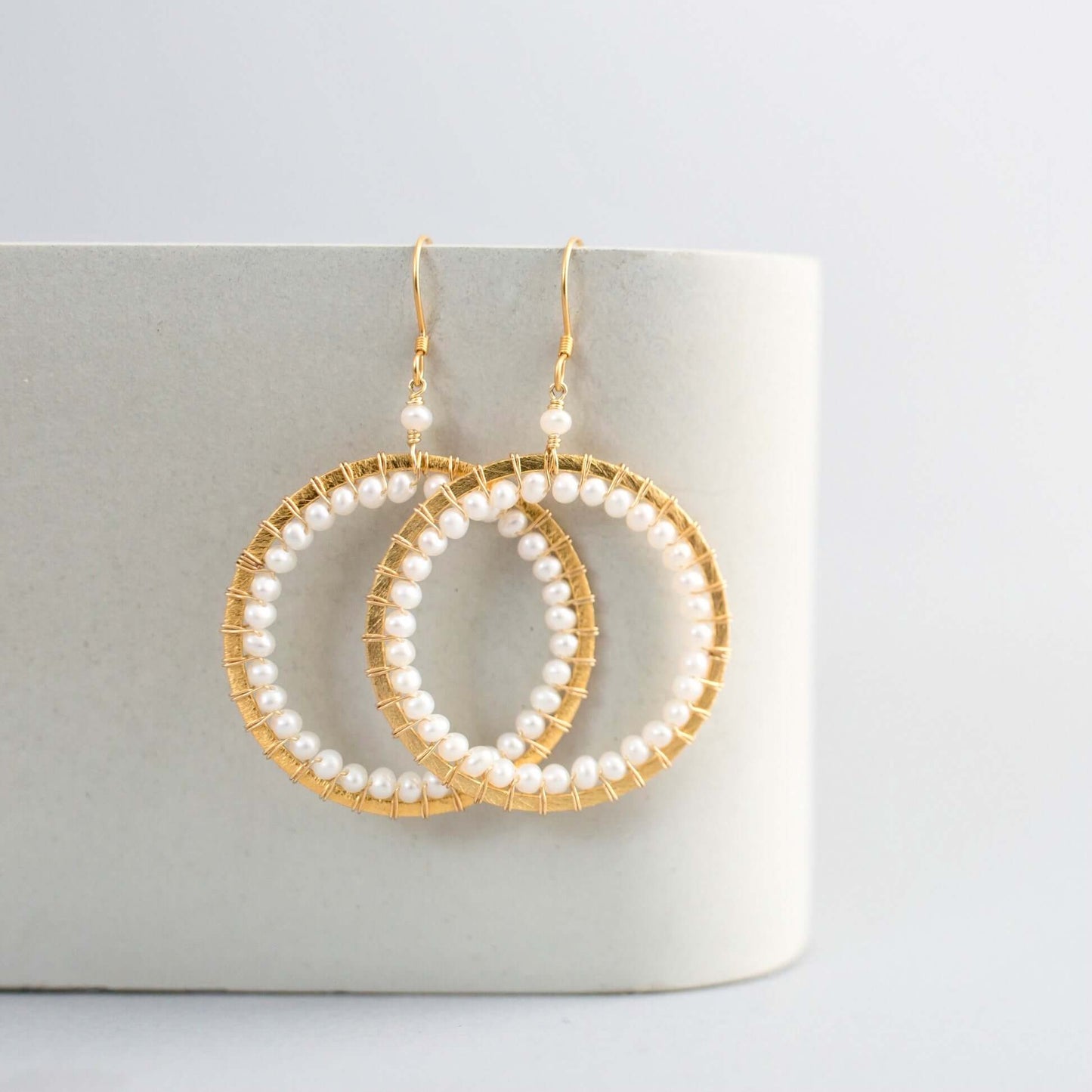 Gold hoop earrings with pearl beads on a light gray background