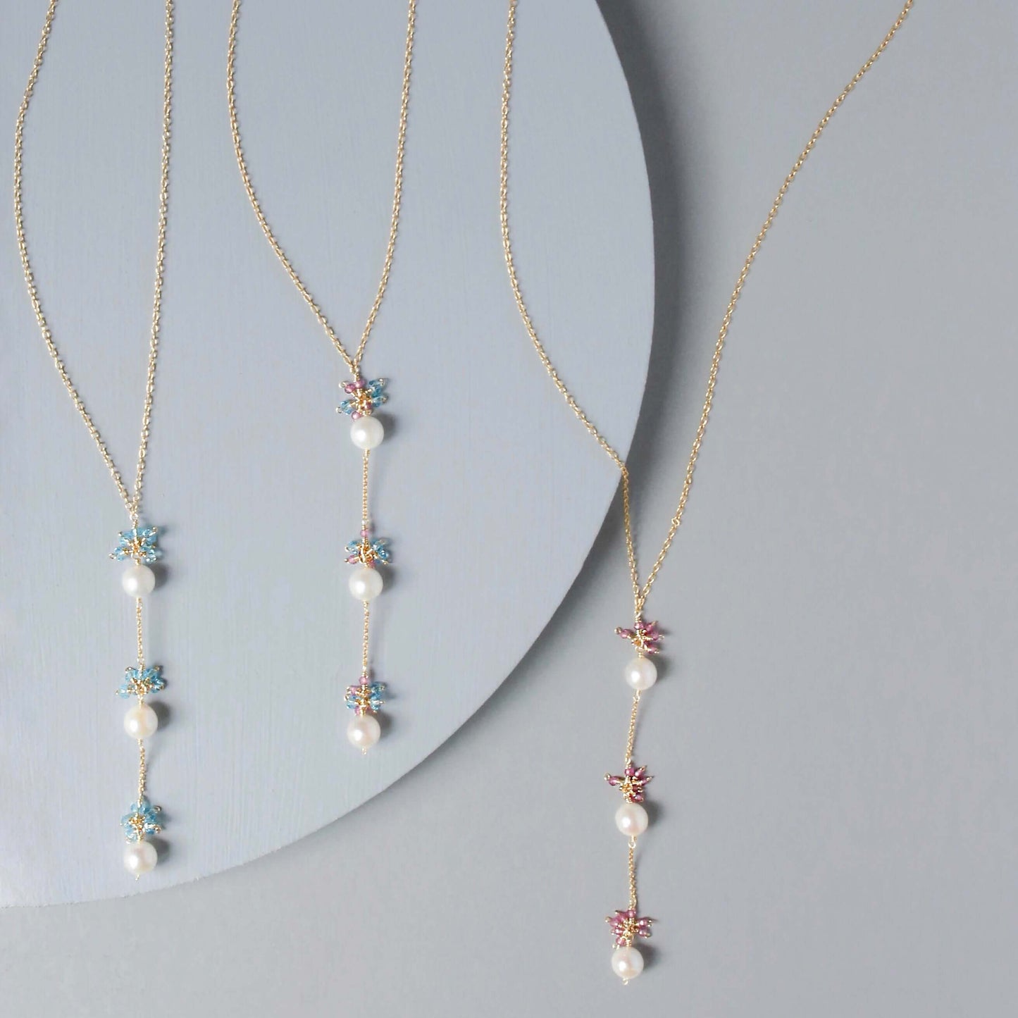 Two pearl necklaces with floral pendants on a gray background