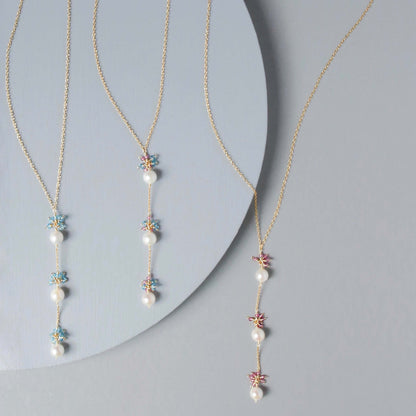 Two pearl necklaces with floral pendants on a gray background