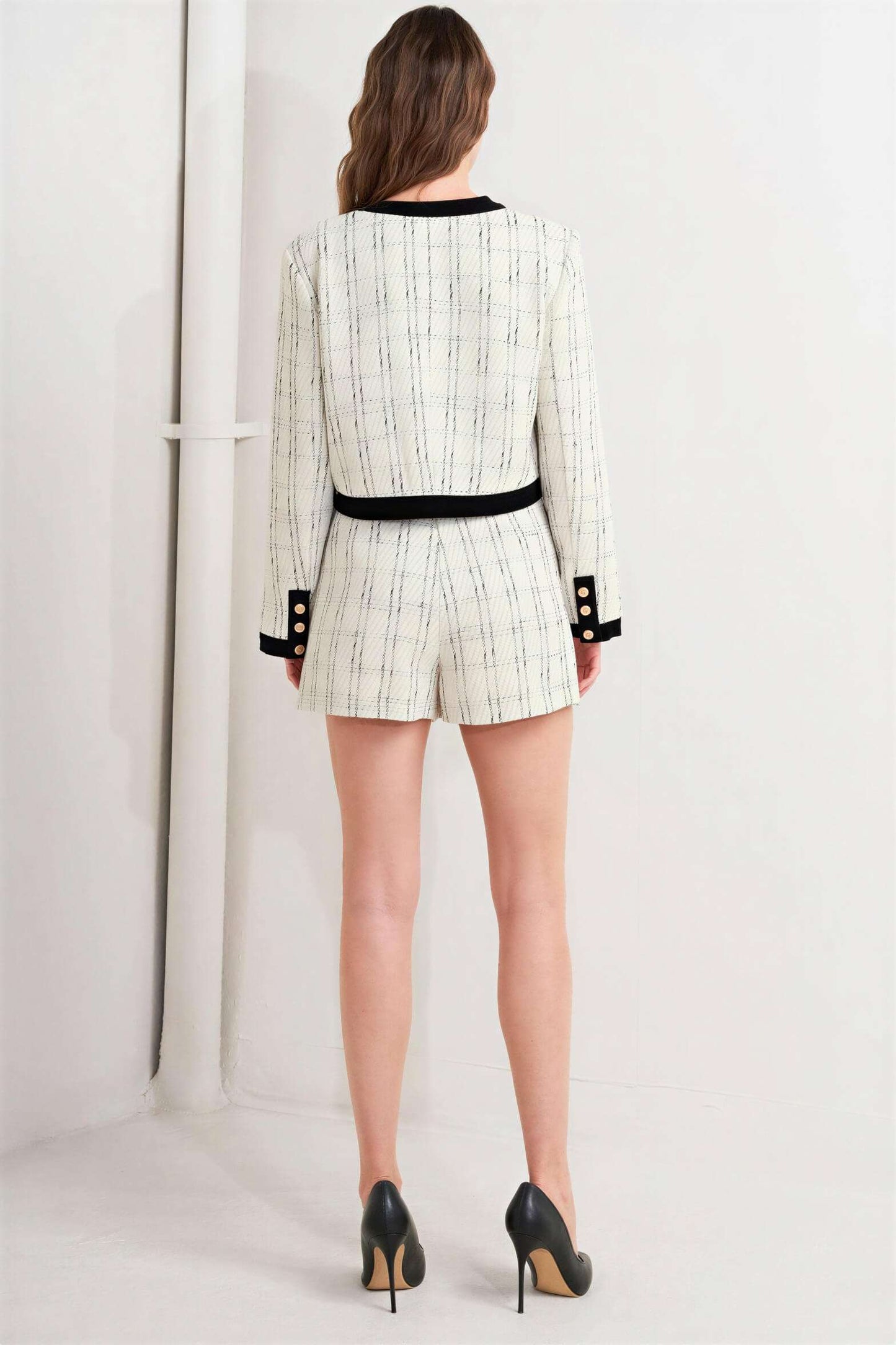 Rear view of a person wearing a white and black patterned fabric jacket and matching shorts with black heels.