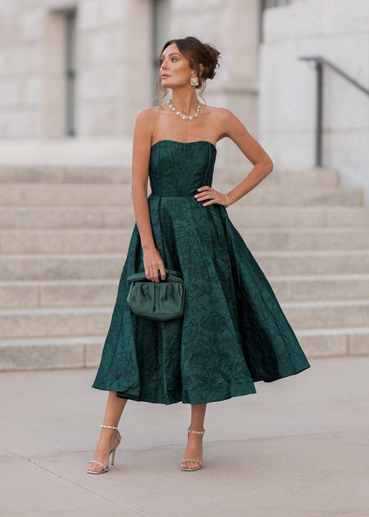 Woman in a strapless green dress standing outdoors with steps and columns in the background