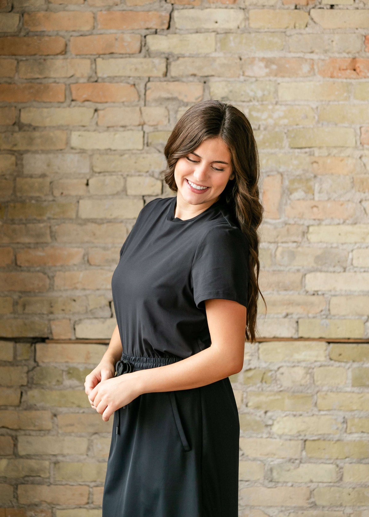 Woman in a black dress standing against a brick wall